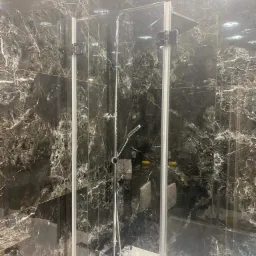 Nowoczesna kabina prysznicowa z czarnymi płytkami imitującymi marmur, chromowana armatura i punktowe oświetlenie sufitowe.