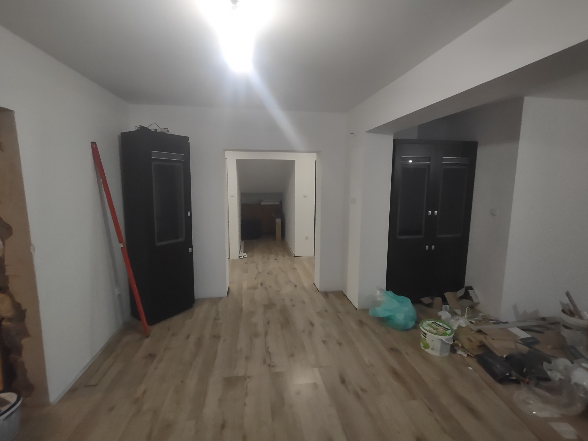 Wnętrze w trakcie prac wykończeniowych: ułożona podłoga z paneli, dwie ciemne szafy po bokach, ściany przygotowane do malowania, widoczne narzędzia i materiały budowlane.