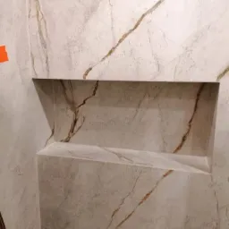 Wykończona wnęka prysznicowa wyłożona płytkami imitującymi marmur z widocznym wzorem żyłkowania w odcieniach brązu i szarości.