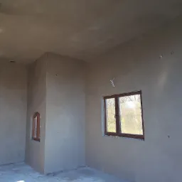 Surowe wnętrze w Nowym Sączu po nałożeniu tynków, z widocznymi drewnianymi oknami i przygotowanymi punktami elektrycznymi.