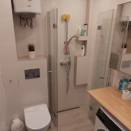 M.C.Remont Michał Ciszek - Nowoczesna, jasna łazienka z kabiną prysznicową ze szklanymi drzwiami, podwieszaną toaletą, bojlerem z motywem żaglówki, pralką z blatem z jasnego drewna oraz panelami podłogowymi w odcieniach beżu.