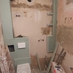 M.C.Remont Michał Ciszek - Wnętrze łazienki w trakcie remontu: widoczne płyty gipsowo-kartonowe na ścianach i suficie, częściowo zamontowana toaleta, drabina oparta o ścianę, narzędzia i materiały budowlane w nieładzie.