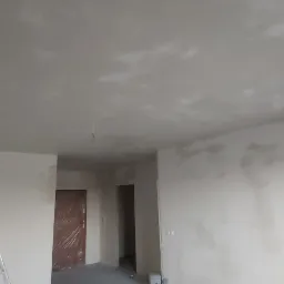 Wnętrze w trakcie remontu: ściany i sufit po szpachlowaniu, widoczne niedoskonałości i miejsca wymagające dalszej obróbki, drabina oparta o ścianę, zabezpieczone folią drzwi w tle.