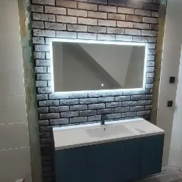 Ukończona łazienka z umywalką w szafce w kolorze morskim, podświetlanym lustrem w ramie z cegły i panelami podłogowymi.