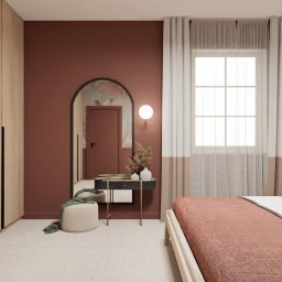 Studio Sto - Sypialnia w odcieniach terakoty z łóżkiem, toaletką z lustrem w kształcie łuku, beżową pufą z zielonym szalem, szafą z jasnego drewna i lampą wiszącą z kulistym kloszem.