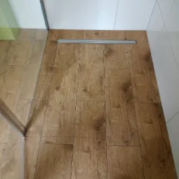 Ułożone panele podłogowe imitujące drewno w kabinie prysznicowej z odpływem liniowym, widok z góry.