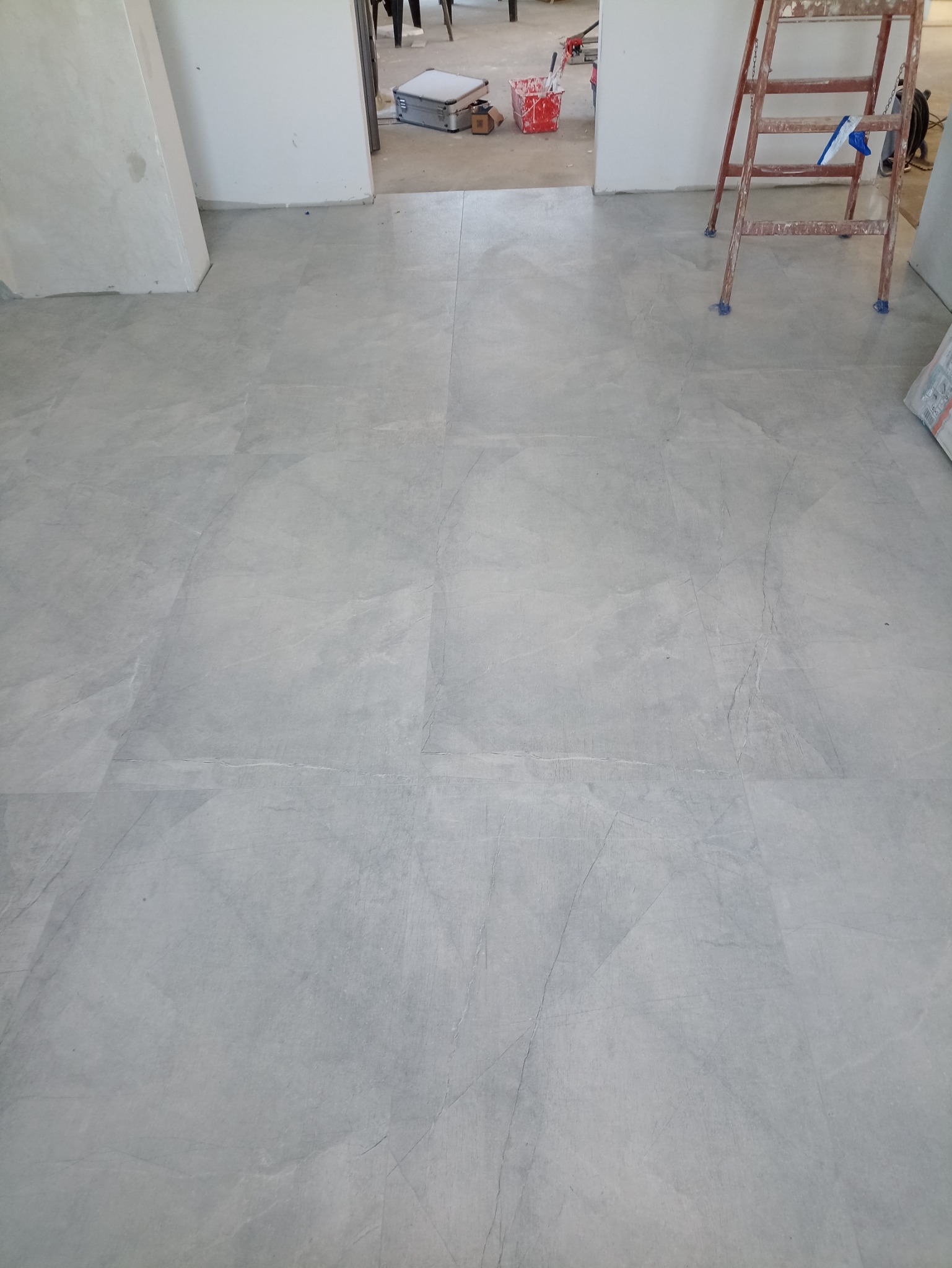 Wykończona podłoga z szarych, marmurkowych płytek w trakcie remontu, widoczna drabina malarska i wiadro z farbą w tle.