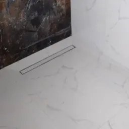 Wykończona łazienka z marmurowymi płytkami na ścianach i podłodze, z odpływem liniowym w rogu.