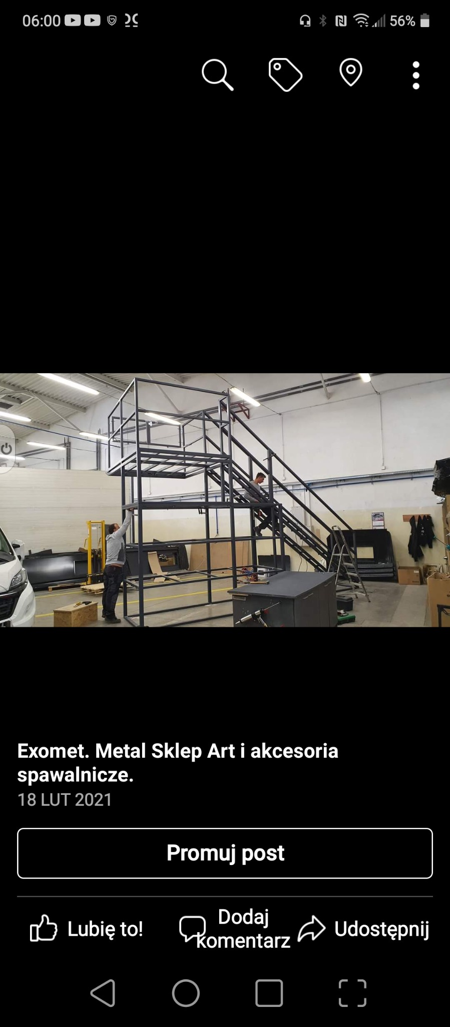 Konstrukcja metalowa z platformą i schodami w hali produkcyjnej, dwóch pracowników przy pracy, oświetlenie sufitowe.