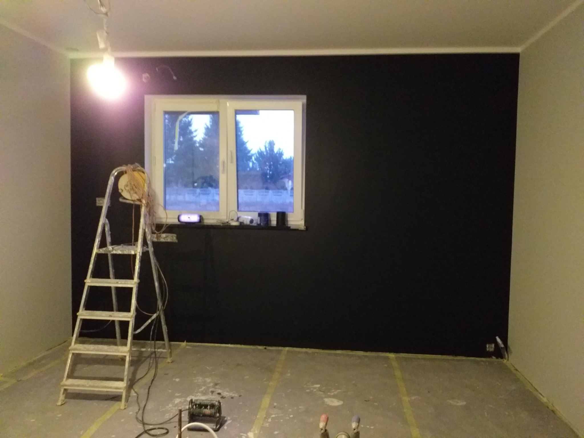 Pokój w trakcie malowania na czarno, drabina malarska z osprzętem, zabezpieczona podłoga, widok na okno.