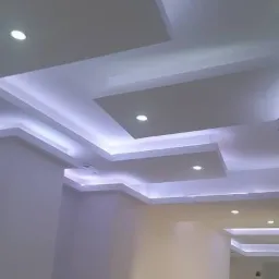 Sufit wielopoziomowy z podświetleniem LED, wnęki o prostokątnym kształcie, centralne oświetlenie punktowe, kremowe ściany, widok z dołu.