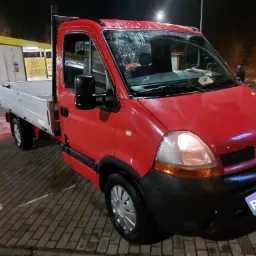 Czerwony samochód dostawczy Renault z otwartą skrzynią ładunkową, zaparkowany nocą przy automatycznej myjni samochodowej.