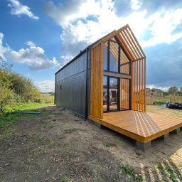 Green Building - Nowoczesny dom modułowy z drewnianą konstrukcją szkieletową i tarasem, widok z zewnątrz w słoneczny dzień.
