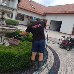 MaR-GaRet firma sprzątająco porządkowa Małgorzata Kasprzykowska - Pracownik w trakcie czyszczenia fontanny myjką ciśnieniową na tle domu z czerwoną dachówką i kostki brukowej. Widoczny sprzęt do mycia ciśnieniowego.