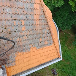 MaR-GaRet firma sprzątająco porządkowa Małgorzata Kasprzykowska - Częściowo wyczyszczony dach z pomarańczowej dachówki karpiówki, widoczne porosty i mech. Na dole sprzęt do czyszczenia pod ciśnieniem i zieleń. Ujęcie z góry.