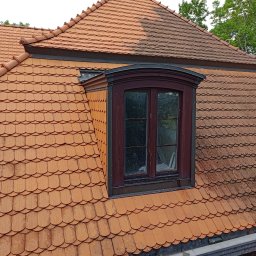 MaR-GaRet firma sprzątająco porządkowa Małgorzata Kasprzykowska - Częściowo wyczyszczony dach z dachówki karpiówki, widoczna lukarna z ciemną ramą okienną. Kontrast czystej i zabrudzonej powierzchni. Ujęcie z dołu, widoczne rynny.