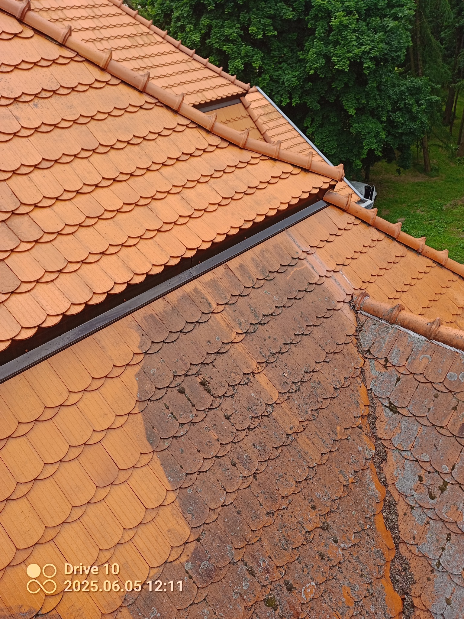 Częściowo wyczyszczony dach z czerwonej dachówki karpiówki, widoczne zabrudzenia i mech. Porównanie stanu przed i po czyszczeniu. Ujęcie z góry, w tle zieleń drzew.