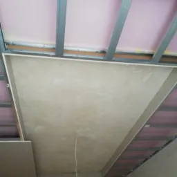 Montaż sufitu podwieszanego z płyt gipsowo-kartonowych na metalowej konstrukcji z widoczną izolacją z wełny mineralnej w trakcie prac wykończeniowych w Krakowie.