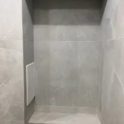 Wykończona wnęka w łazience, wyłożona szarymi płytkami imitującymi marmur, z widocznym panelem rewizyjnym i fragmentem stelaża podtynkowego WC.