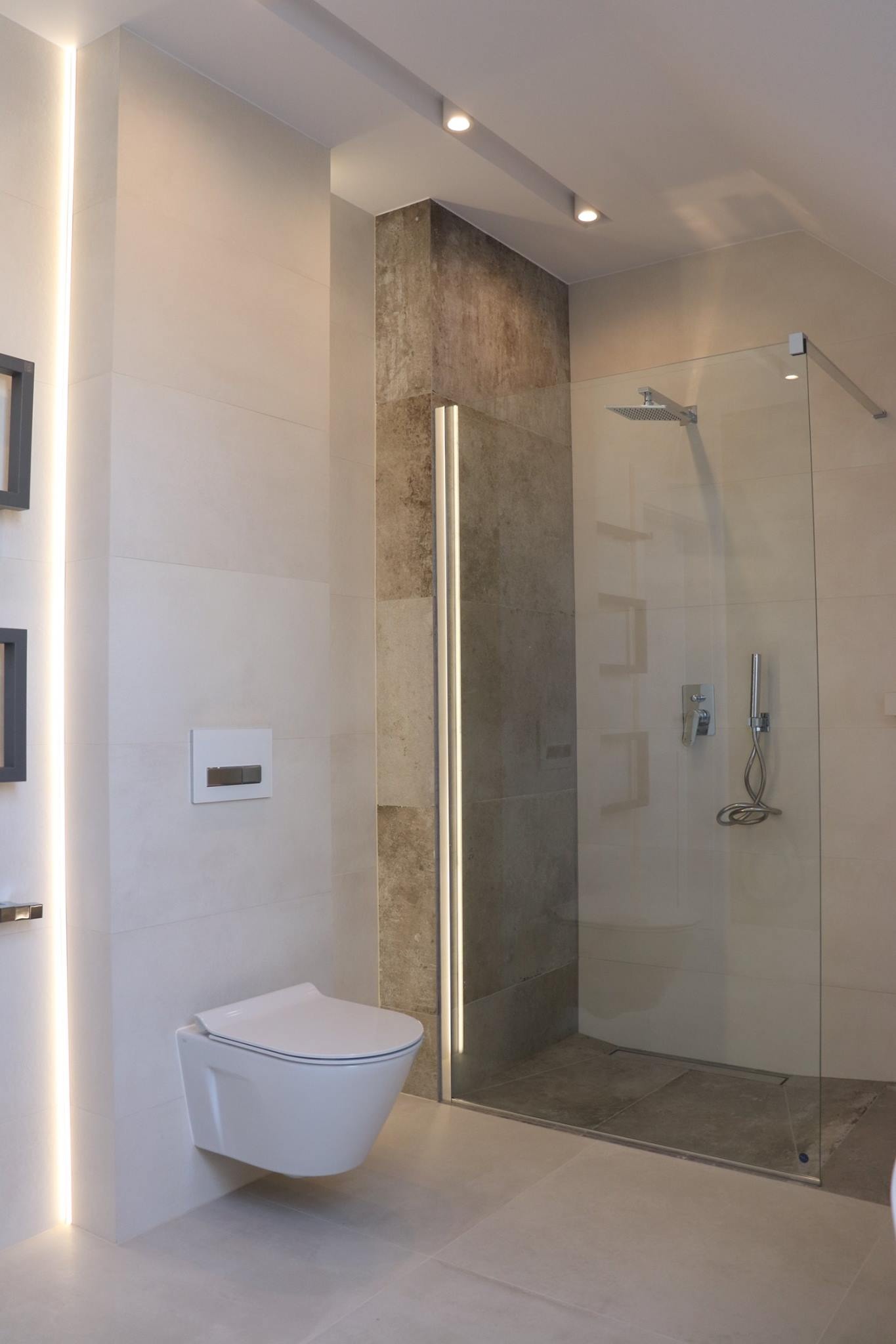 Nowoczesna łazienka z podwieszaną toaletą, szklaną kabiną prysznicową typu walk-in i oświetleniem LED w pionowych profilach.