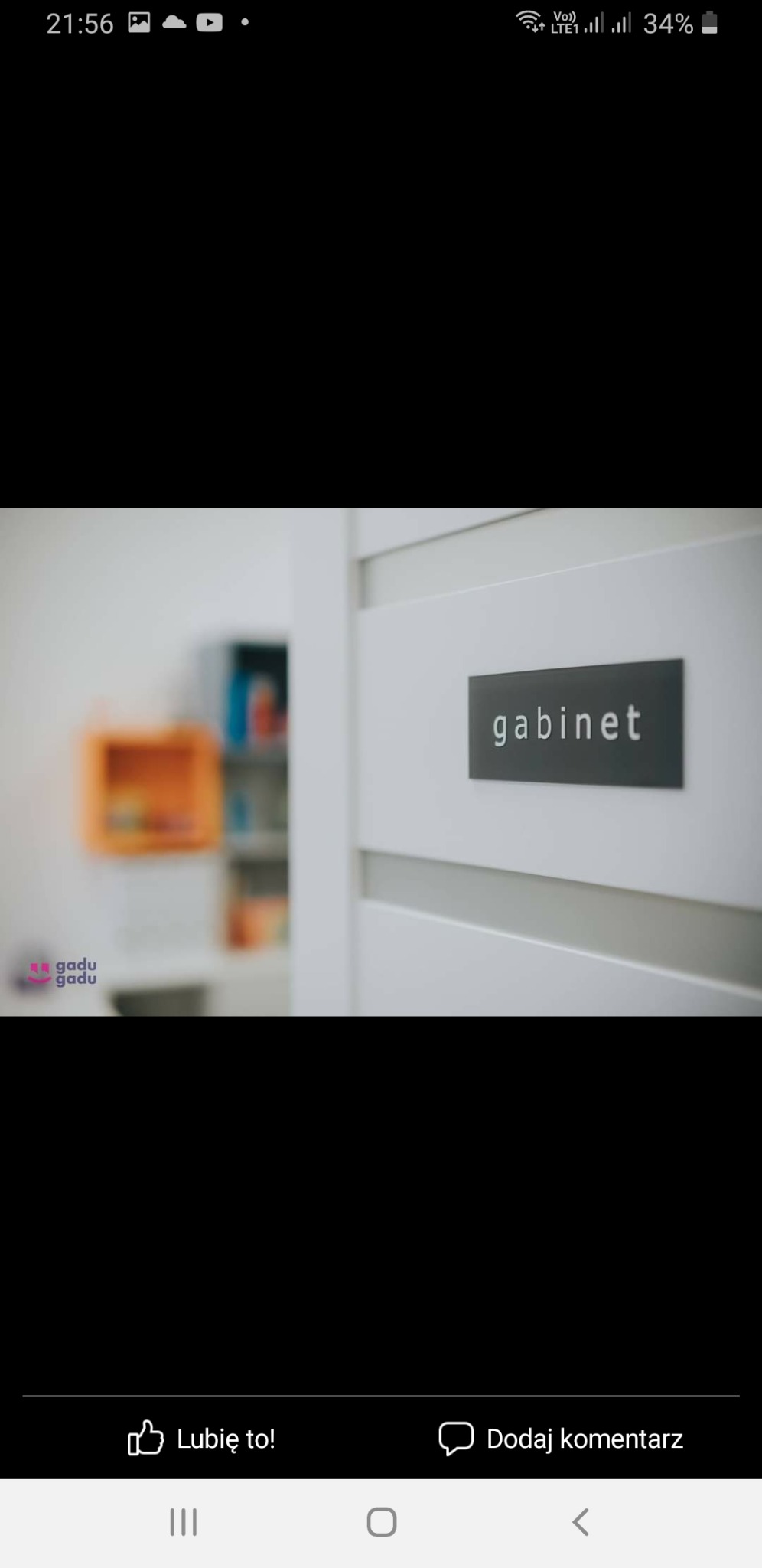 Białe drzwi z szarą tabliczką z napisem 'gabinet' i rozmazane wnętrze z kolorowymi półkami w tle.