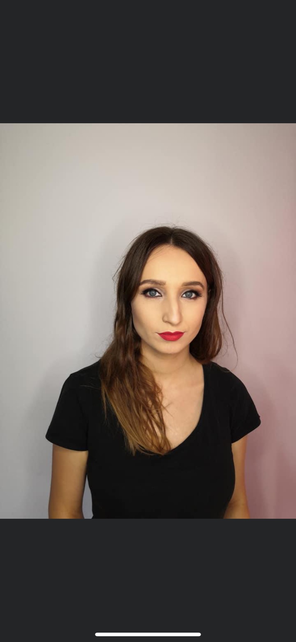 Portret kobiety z profesjonalnym makijażem: wyraziste oczy z ciemnymi cieniami, precyzyjnie podkreślone brwi i intensywnie czerwone usta, na tle jasnej ściany.