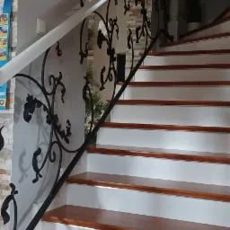 Drewniane schody z białymi podstopnicami i ozdobną, kutą balustradą w ciemnym kolorze, widok z dołu, jasne wnętrze.