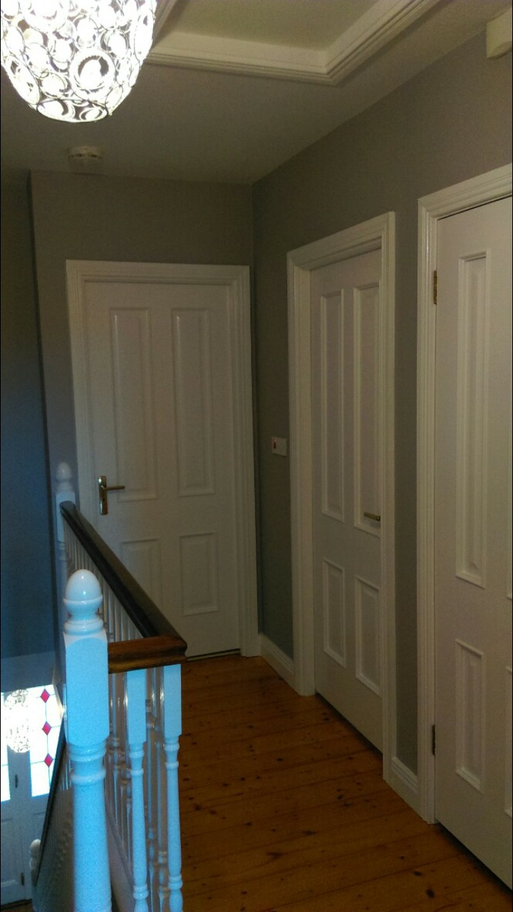 Korytarz po remoncie z trzema białymi drzwiami, szarymi ścianami i drewnianą podłogą, widok z góry schodów.