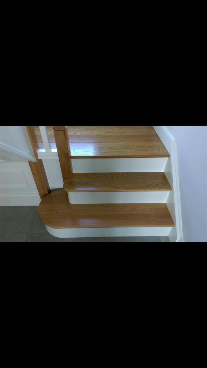 Drewniane schody z białymi podstopnicami, zaokrąglony pierwszy stopień, widok z dołu.