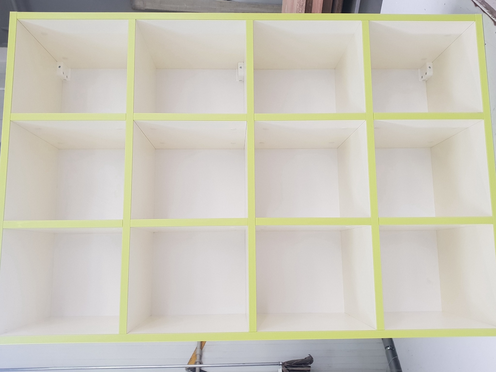 Półki regału z białymi przegródkami i jasnozielonymi krawędziami, widoczne mocowania w niektórych przegródkach, ujęcie z dołu.