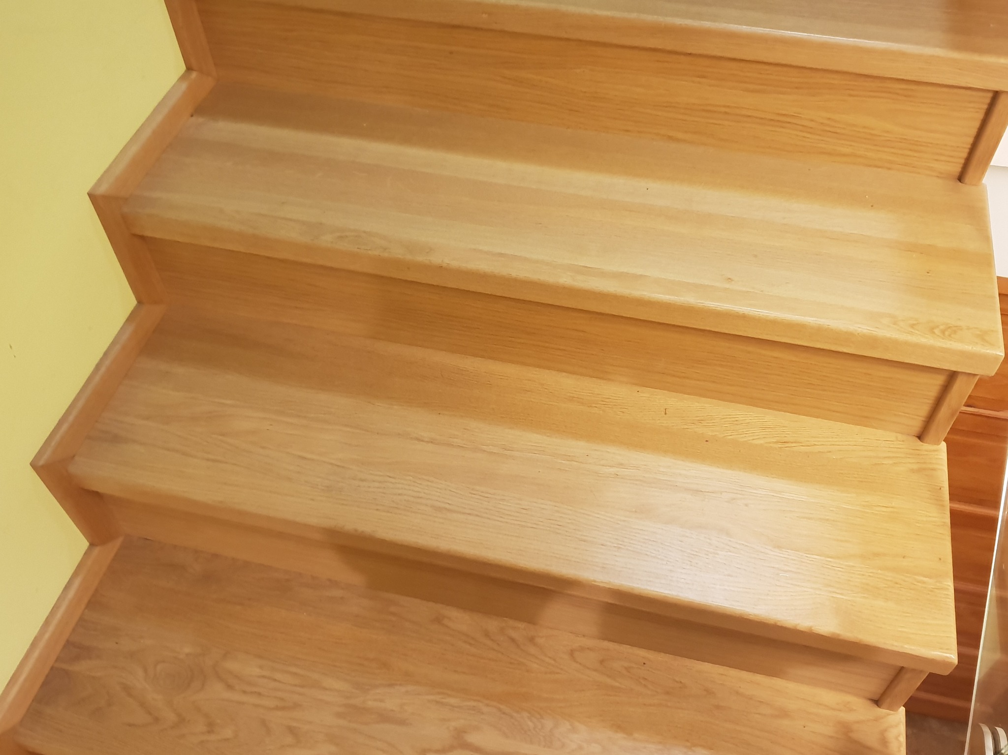 Fragment drewnianych schodów z jasnego drewna dębowego, widok z góry, żółta ściana w tle.