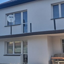 AD-BUD Adrian Matkowski - Biała elewacja domu po malowaniu, widoczne okna, antena satelitarna, rusztowanie z boku i częściowo zasłaniający kadr samochód dostawczy.