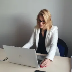 Kobieta w białej marynarce i okularach pracuje na laptopie Dell przy biurku w biurze.