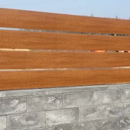 Nowoczesne ogrodzenie z paneli imitujących drewno w kolorze brązowym i czarnym, wsparte na szarych, betonowych słupkach i podmurówce z bloczków.