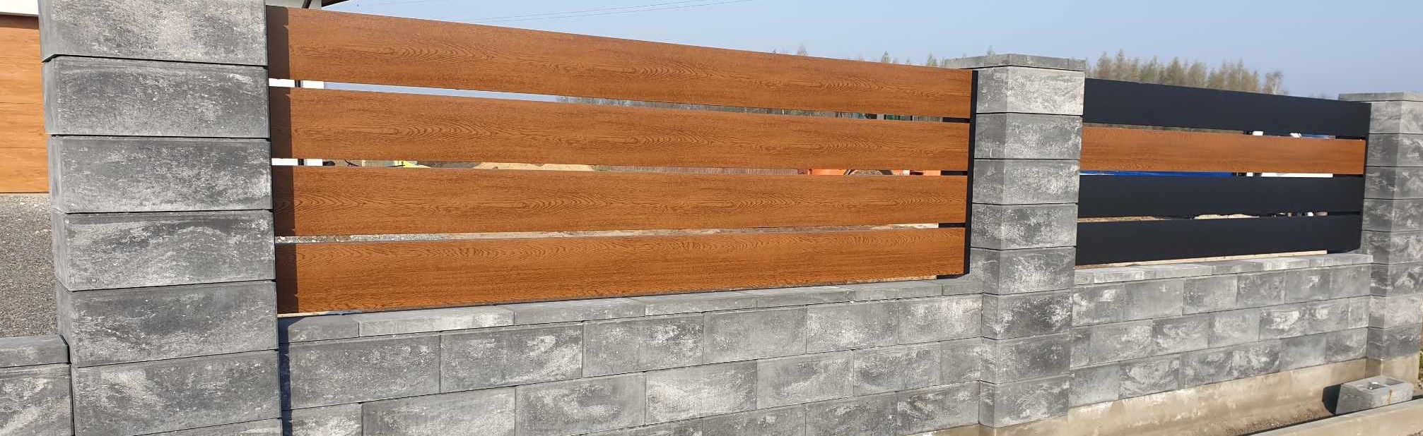 Nowoczesne ogrodzenie z paneli imitujących drewno w kolorze brązowym i czarnym, wsparte na szarych, betonowych słupkach i podmurówce z bloczków.