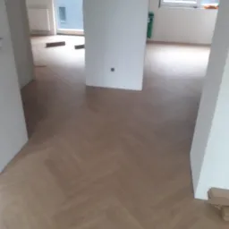 Świeżo położona, jasna podłoga drewniana w jodełkę klasyczną w nowym mieszkaniu, widoczne fragmenty kartonów po panelach przy ścianie.