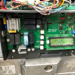 Otwarta obudowa centrali sterującej bramy CAME ZBK10, widoczna zielona płytka drukowana z elementami elektronicznymi, wyświetlaczem LCD pokazującym adres strony internetowej producenta i okablowaniem.