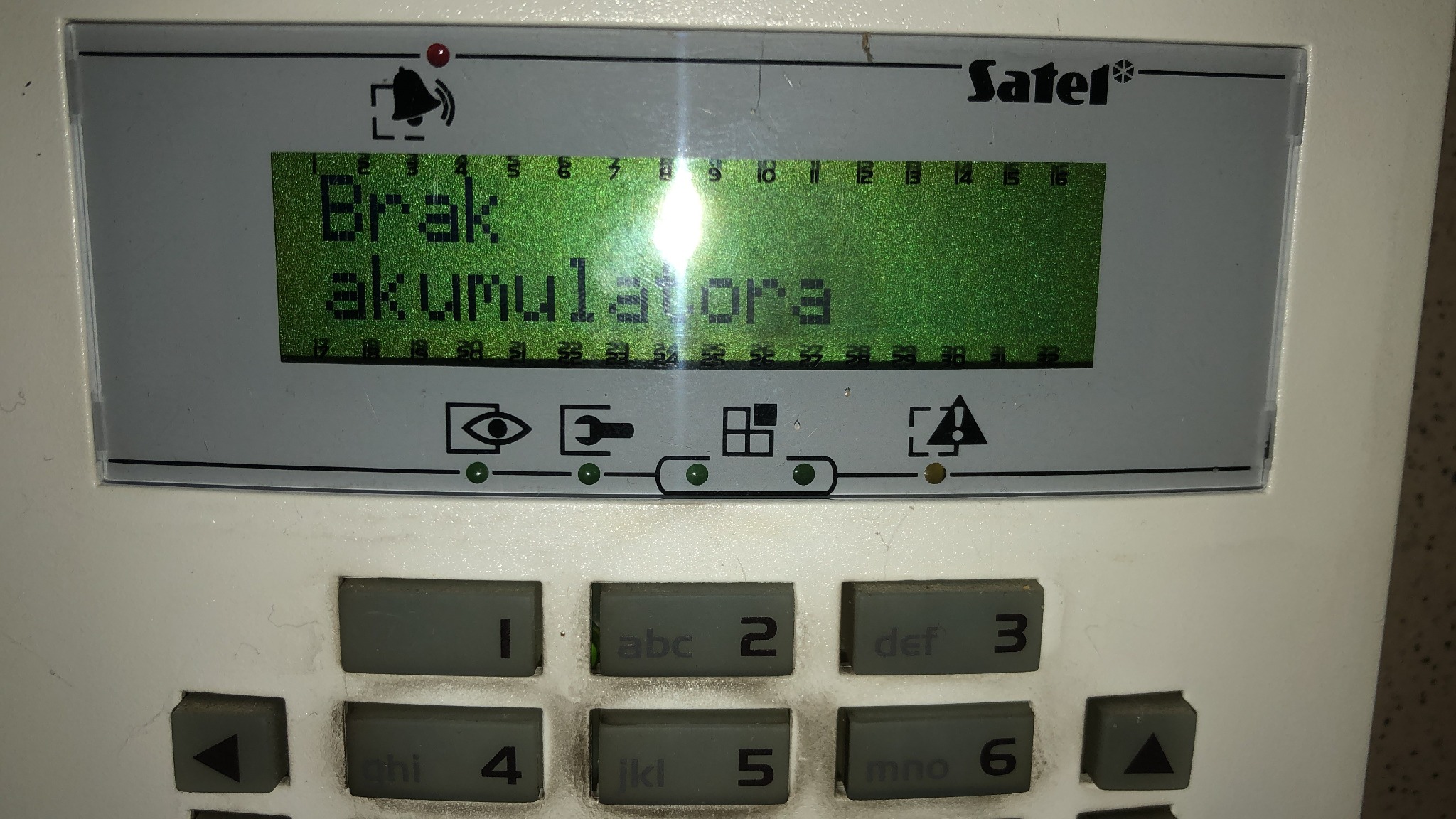 Panel alarmowy Satel wyświetlający komunikat 'Brak akumulatora' na zielonym ekranie LCD, widoczne przyciski numeryczne i funkcyjne, obudowa z widocznymi śladami użytkowania.