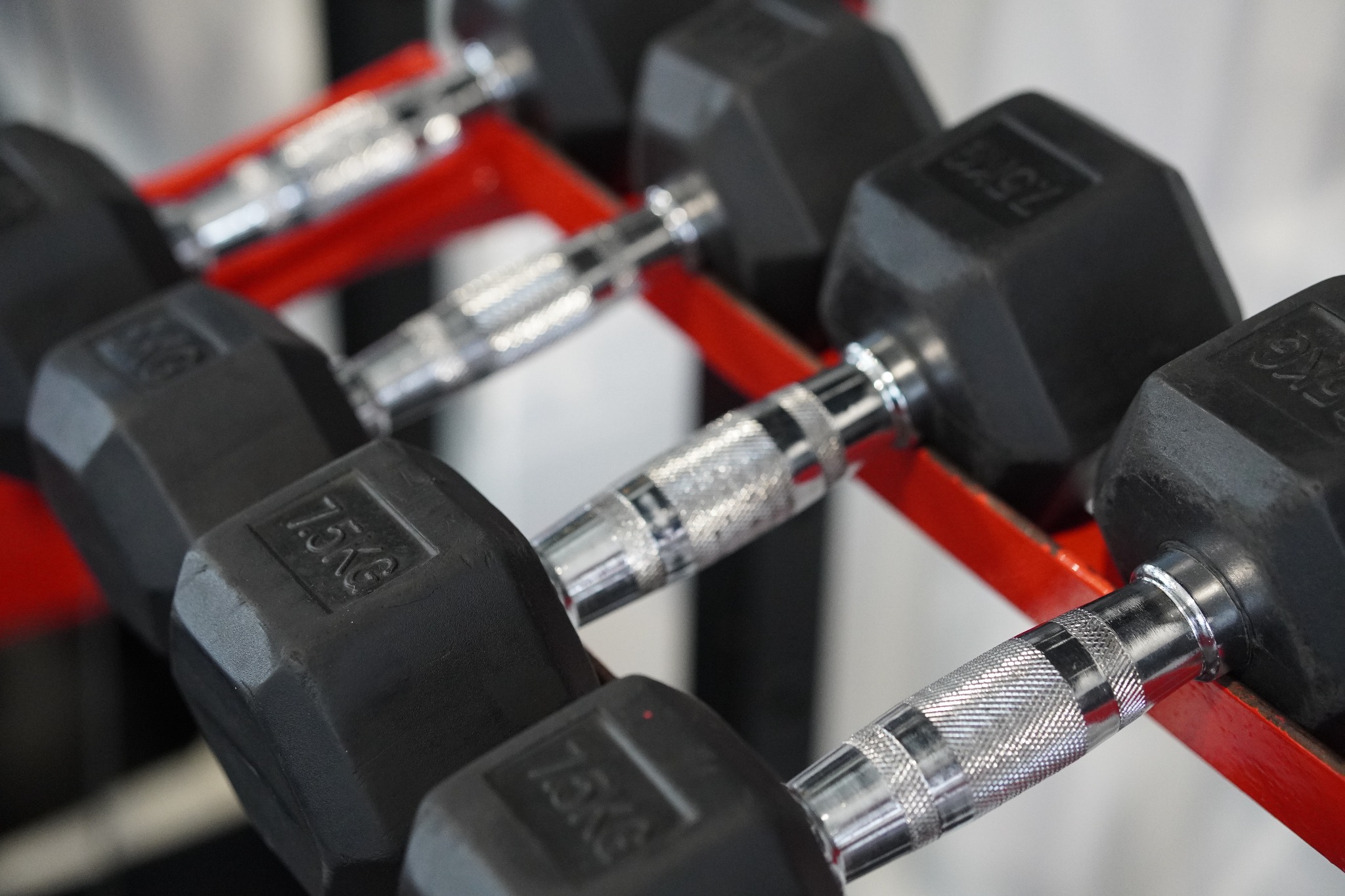 Rząd czarnych hantli 7.5 kg na czerwonym stojaku, uchwyty z radełkowaną powierzchnią.
