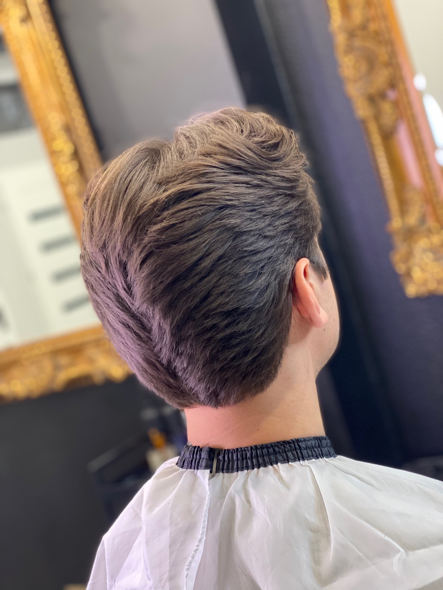 Męska fryzura z widocznym cieniowaniem, wykonana w salonie z ozdobnym, złotym lustrem w tle.