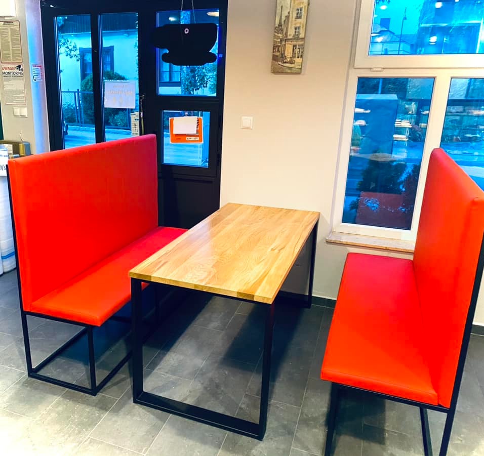 Stół z jasnego drewna i dwie czerwone ławki z czarnymi metalowymi nogami w pomieszczeniu z oknem.