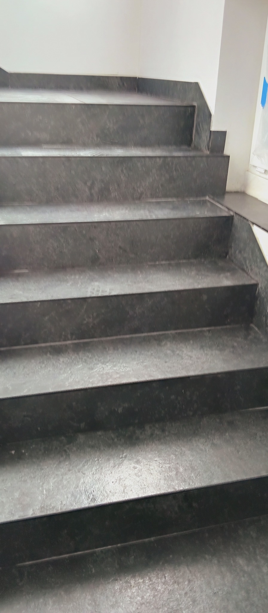 Granitowe schody wewnętrzne z ciemnego kamienia, widok z dołu, ukazujący detale wykończenia i strukturę materiału. Minimalistyczny design w nowoczesnym wnętrzu.