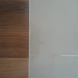 Połączenie brązowych paneli podłogowych z jasnymi, kwadratowymi płytkami ceramicznymi na ścianie, widoczne fugi.