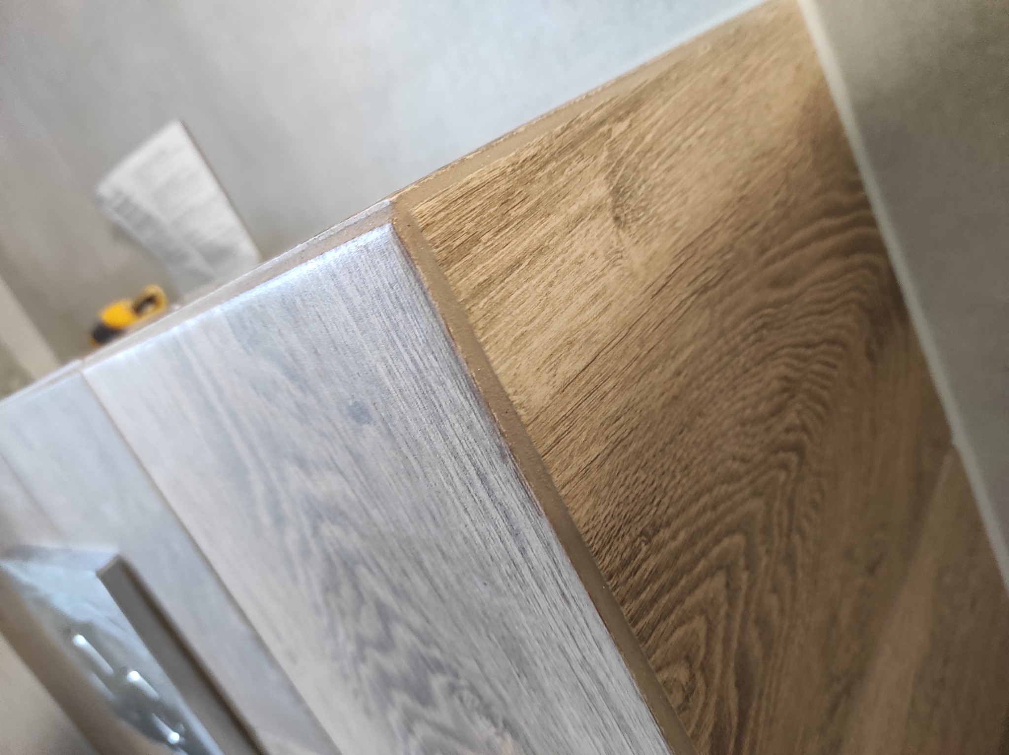 Połączenie dwóch rodzajów paneli podłogowych: szarego i dębowego, z widoczną listwą przypodłogową i fragmentem narzędzia w tle.