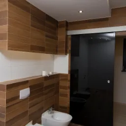 Nowoczesna łazienka z brązowymi płytkami imitującymi drewno, białymi sanitariatami i czarnymi, przesuwnymi drzwiami szklanymi.