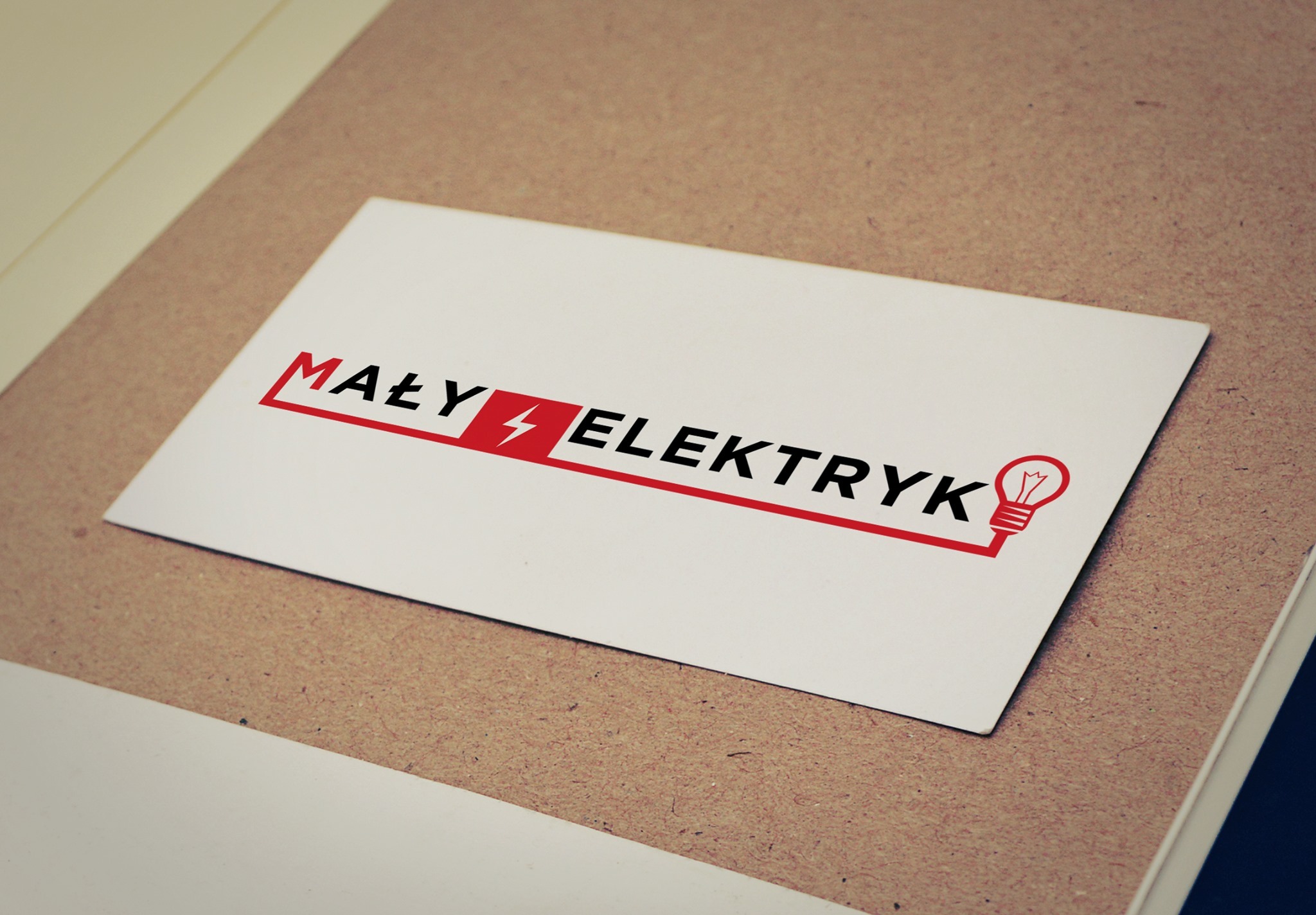 Wizytówka z logo firmy 'Mały Elektryk' na tekturowym podłożu, z czerwonym akcentem w postaci obramowania napisu i symbolu żarówki.