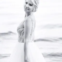 Portret kobiety w balowej sukni z cekinami, z delikatnym uśmiechem, na tle morza w czerni i bieli, z włosami upiętymi w kok.
