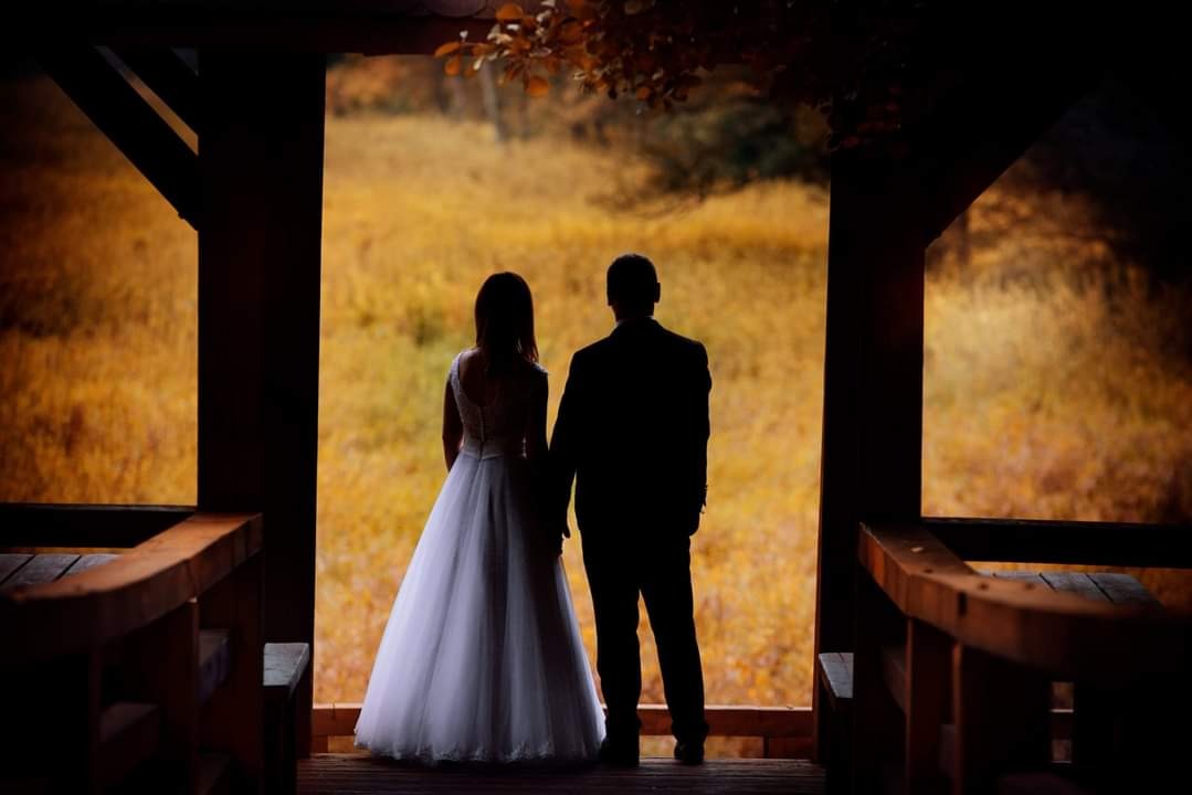 Para młoda, sylwetki na tle jesiennego krajobrazu, stoją na drewnianym podeście, trzymając się za ręce, widok z tyłu.