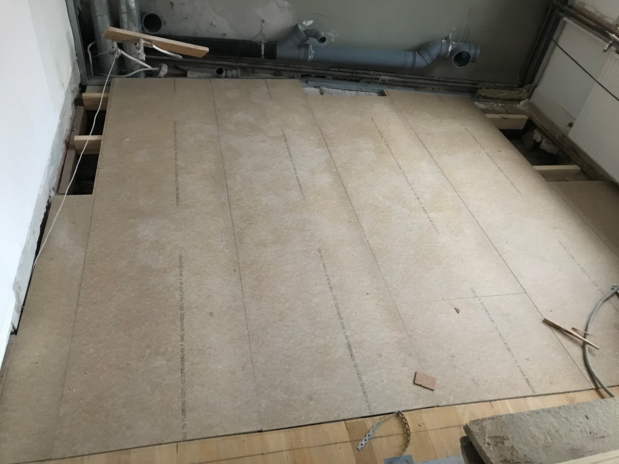 Przygotowanie podłoża pod nową podłogę: płyty OSB ułożone na drewnianych legarach, widoczne instalacje pod sufitem.