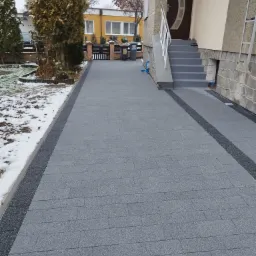 Szara kostka brukowa ułożona przed domem z elementami zimowego krajobrazu i świeżym śniegiem.